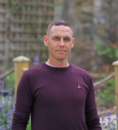 Portrait photo of Anthony Deegan, Recovery Advocate at Smarmore Castle, photo taken outside with a garden and flowers in the background