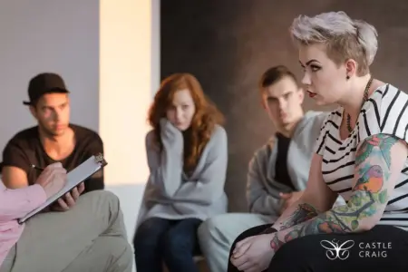 Group therapy session with four people sitting in a circle and a woman with tattoos talking to a therapist