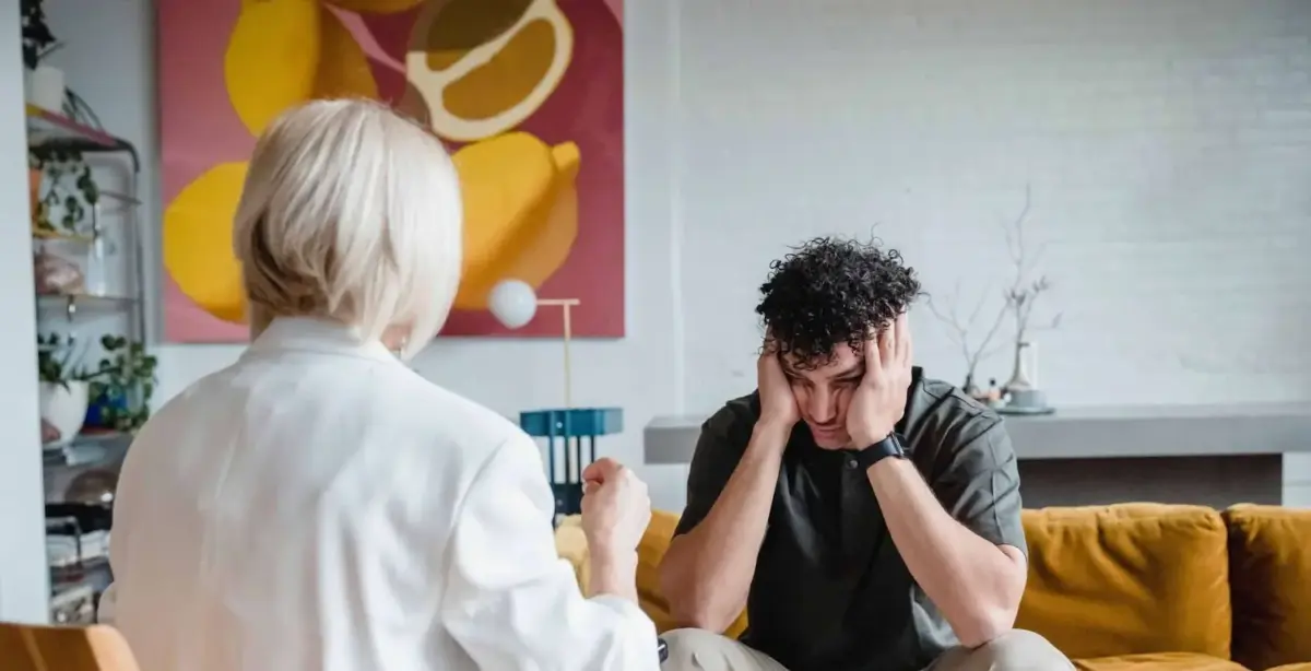 Man in a therapy session holds his head in his hands while a therapist talks to him