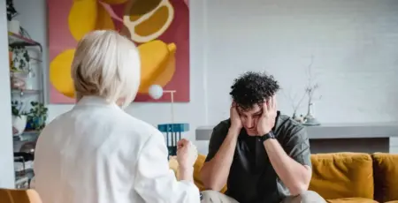 Man in a therapy session holds his head in his hands while a therapist talks to him