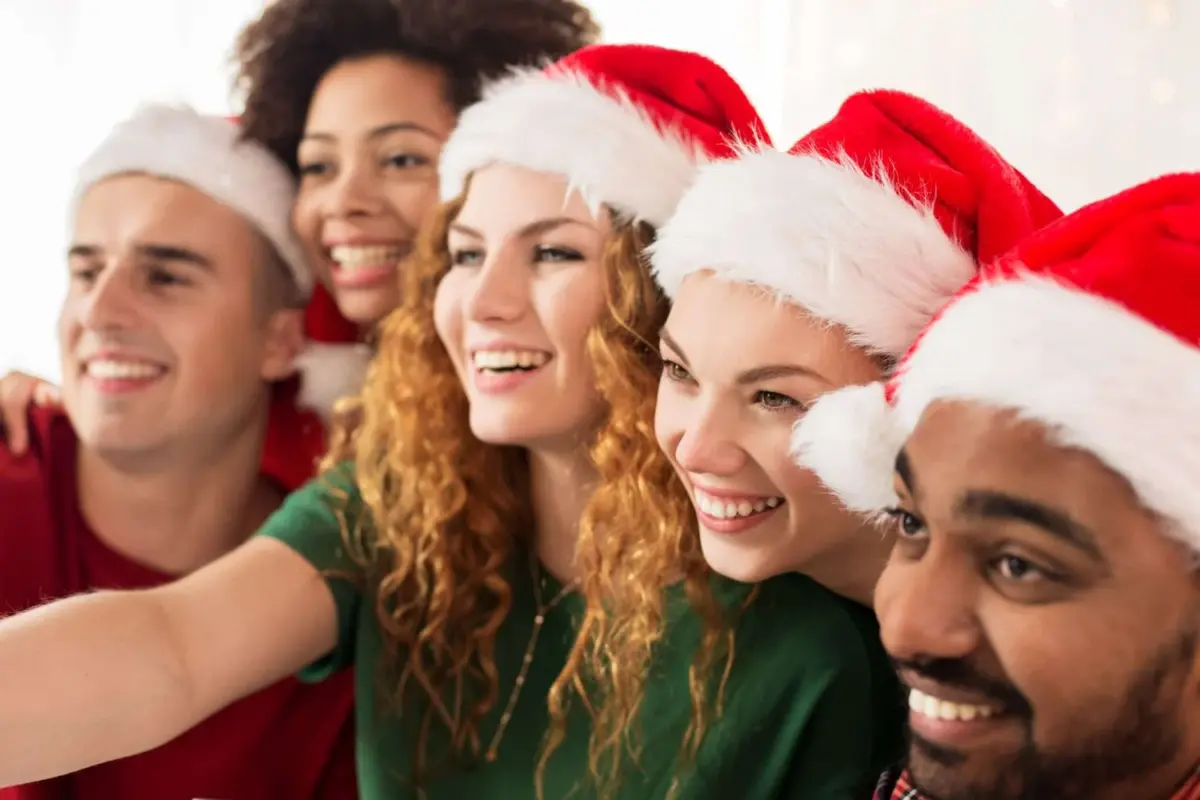 A group of people pose together for a photo, some wearing red and white santa claus hats