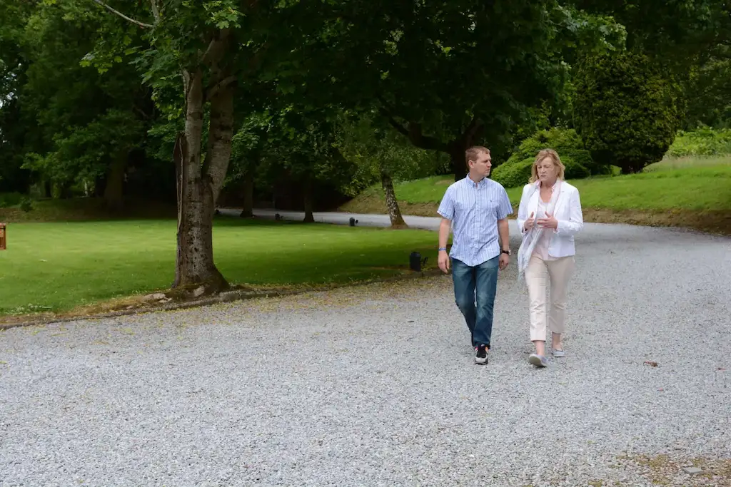 Two people, a patient and an addiction therapist, talking while walking up a stone path surrounded by trees at Smarmore Castle