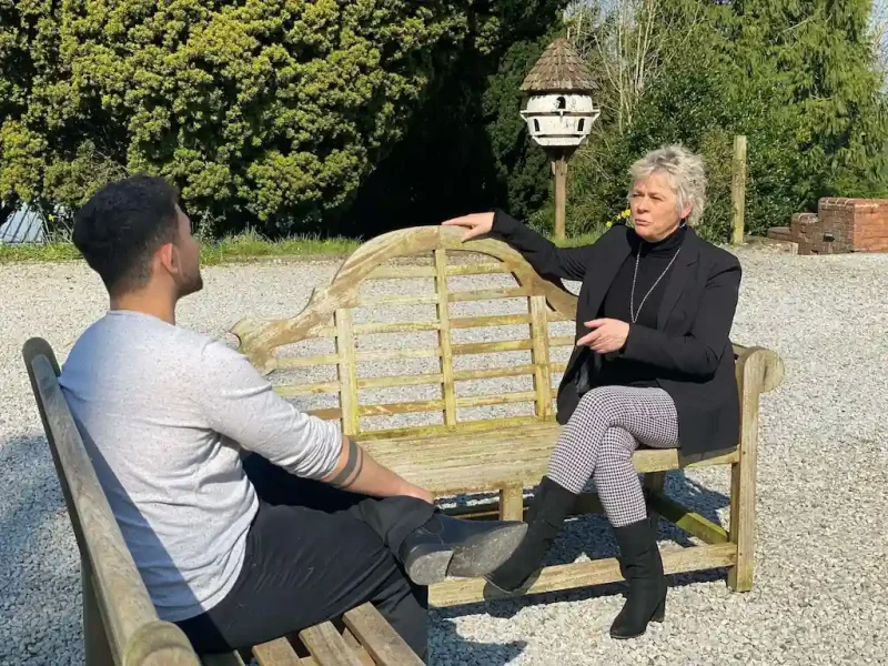 Two people talking outside in the sunshine sitting on benches that face one another at Smarmore Castle in Ireland