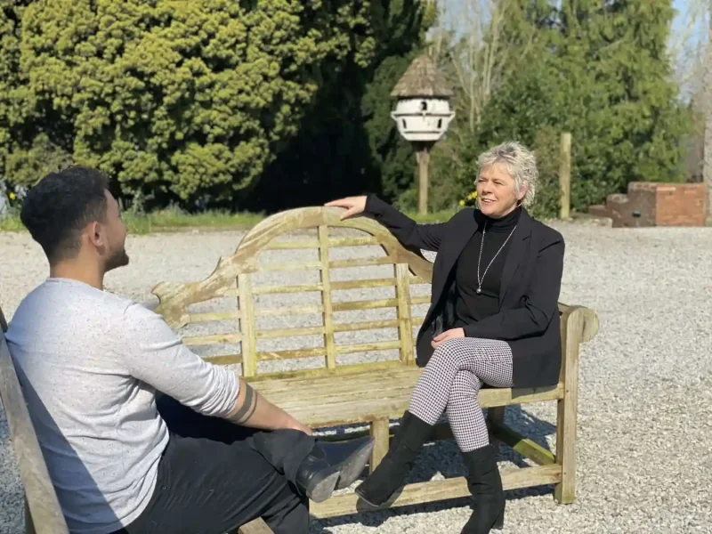 Two people talking while sitting outside in the sunshine on benches that face one another at Sarmore Castle in Ireland
