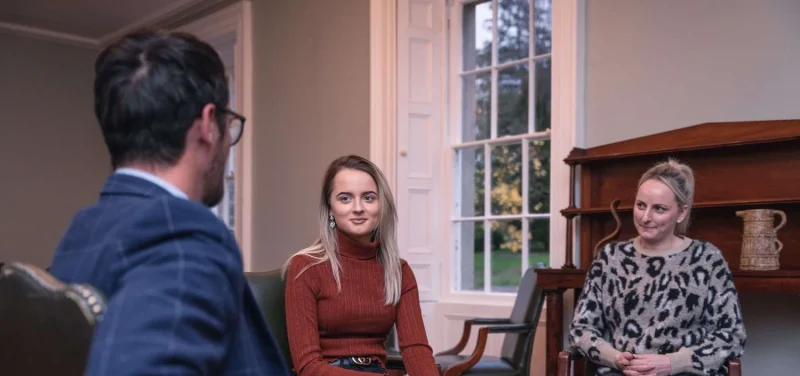 Three people sit in chairs inside talking at Smarmore Castle Private Rehab Clinic