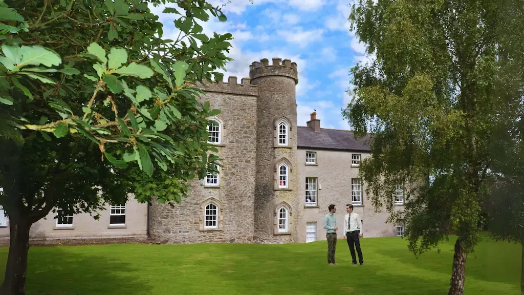 Outdoor image of Smarmore Castle framed by trees with two people standing on the grass in front of the building, talking