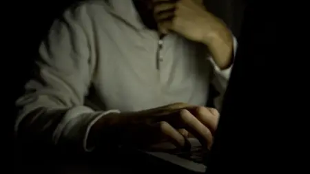 An anonymous man sitting at a laptop in the dark considering getting help with gambling addiction.