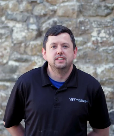Portrait photo of Liam McQuillan, kitchen assistant at Smarmore Castle, photo taken outside against a stone wall background