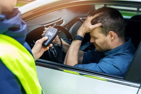 A man in the car holding his head after doing a breathalyser and learning about the dangers of drink driving.
